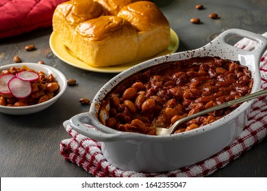 Baked Beans In Bbq Sauce With Dinner Rolls In The Background. Close Up.