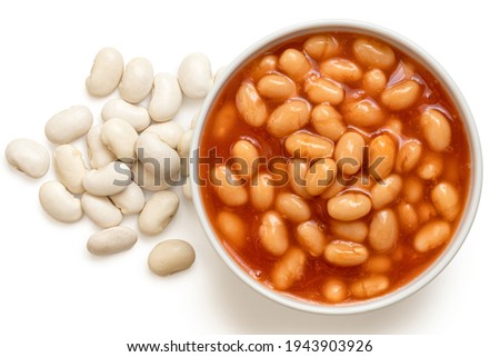 Baked beans in tomato sauce in a white ceramic bowl next to uncooked haricot beans isolated on white. Top view.