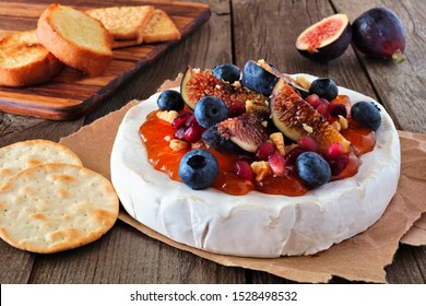 Baked Brie Appetizer With Figs And Jam, Blueberries, Pomegranates And Nuts. Side View On A Rustic Wooden Table.