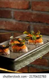baked bruschetta with salmon, cheese, sun-dried tomatoes and avocado in gray plate on bright background.