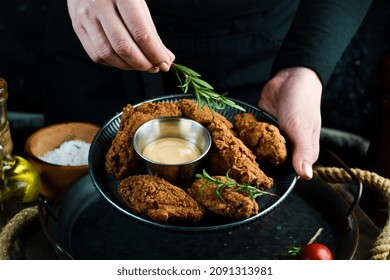 Baked Buffalo Chicken Wings On A Plate In The Hands Of A Chef On A Black Background.