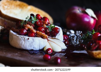 Baked Camembert Brie cheese with a cranberry, honey, balsamic vinegar and nut relish and garnished with thyme. Served with toasted bread slices. Selective focus with blurred background and foreground.