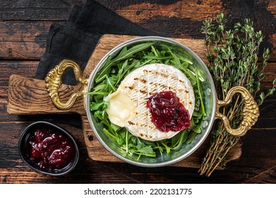 Baked Camembert Brie cheese with a cranberry sauce and garnished with arugula salad in a skillet. Wooden background. Top view.