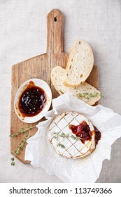 Baked Camembert cheese with thyme and toasted bread on wooden board