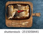 Baked carp fish fillet with red chili pepper and spices in glass baking dish on chopping board, close up, top view