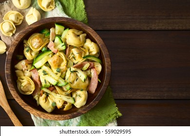 Baked cheese tortellini or belly button pasta with zucchini, bacon and thyme in wooden bowl, photographed overhead on dark wood with natural light (Selective Focus, Focus on the top of the dish)