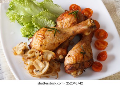 Baked chicken drumsticks with mushrooms and tomatoes on a plate. horizontal view from above 