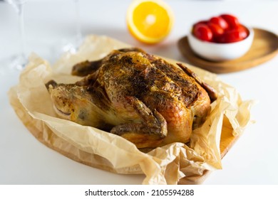 Baked chicken with spices in parchment paper on a wooden board, with orange and cherry tomatoes in the background