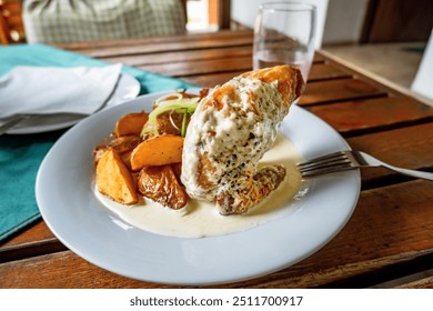 Baked chicken wing with white cheese sauce, sprinkled with green onion circle, baked potato on white plate on wooden table, glass of water. - Powered by Shutterstock