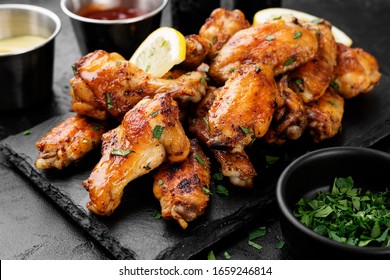 Baked chicken wings served with different sauces and lemon. Black background