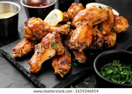 Baked chicken wings served with different sauces and lemon. Black background