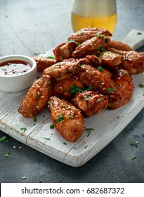 Baked chicken wings with sesame seeds, beer and sweet chili sauce on white wooden board.