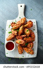 Baked chicken wings with sesame seeds and sweet chili sauce on white wooden board.