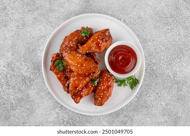 Baked chicken wings in a sweet chili sauce and sesame seeds on a white plate on a concrete background. Top view, copy space