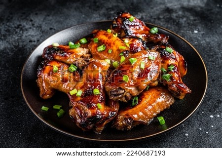 Baked chicken wings with sweet chili sauce in a plate. Black background. Top view.