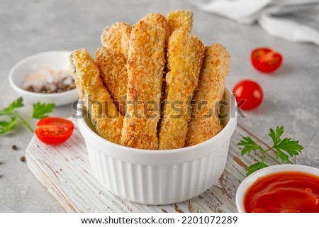 Baked crispy garlic parmesan zucchini sticks served with tomatoes sauce on a gray concrete background. Vegetarian healthy dish. Selective focus