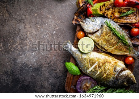 Baked Dorado fish, sea bream with grilled vegetables, herbs and seasonings, top view