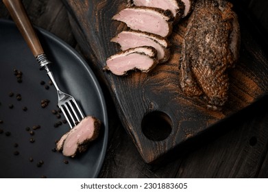 Baked duck fillet. Sliced poultry meat. Piece of duck on fork. Meat onwooden cutting board. Wooden background. View from above. Soft focus. 