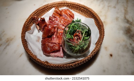 A Baked Duck With Green Salad In A Straw Plate