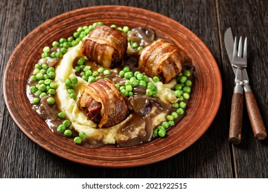baked faggots served with creamy mashed potatoes, green peas and rich, thick onion gravy on a clay plate, british cuisine