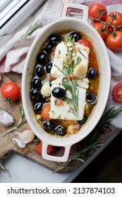 Baked feta cheese with tomatoes, olives, garlic, oil, honey and rosemary in baking dish on a rustic background
