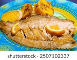 Baked flounder fish with onion, lemon and potatoes. Close-up.