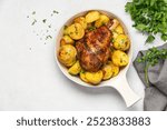 Baked golden turkey leg with potatoes in ceramic dish on light table with copy space