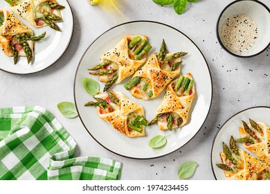 Baked green asparagus with ham and cheese in puff pastry sprinkled with sesame seeds and green basil leaves. Light gray stone background. top view - Shutterstock ID 1974234455