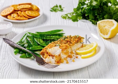 Baked Haddock with Crackers butter toppings served with boiled snow peas and lemon on white plate on white wood table with ingredients Foto d'archivio © 