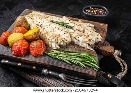 Baked Haddock fish fillet on wooden board with tomato and potato. Black background. Top view Foto stock © 