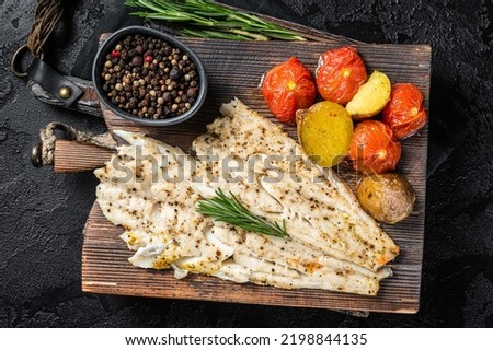Baked Haddock fish fillet on wooden board with tomato and potato. Black background. Top view. Foto stock © 