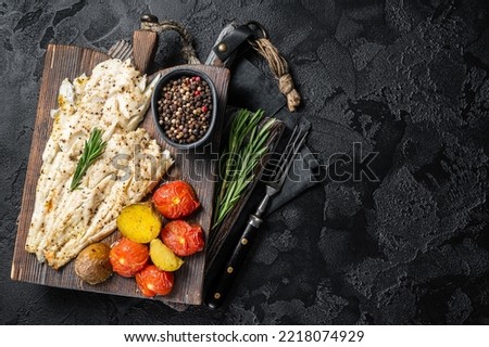 Baked Haddock fish fillet on wooden board with tomato and potato. Black background. Top view. Copy space. Foto stock © 