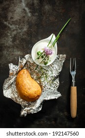 Baked Jacket Potato Cooked Over A Summer Barbecue In Aluminium Foil Served With Fresh Chopped Chives And Sour Cream For A Delicious Appetizer, Overhead View