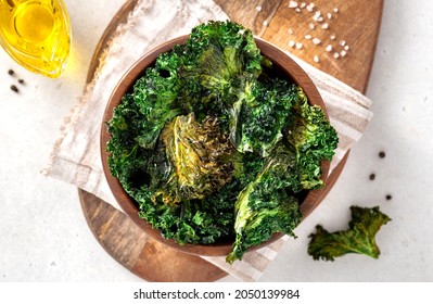 Baked kale chips in a wooden bowl on a light background. Top view. Chips from the leaves of kale cabbage close-up. Kale chips with olive oil and salt, a tasty vegan snack.  - Powered by Shutterstock