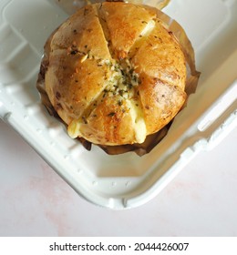 Baked Korean Cream Cheese Garlic Bread Over Aluminum Foil Baking Sheets Contained In Biodegradable Leakproof Take Out Food Boxes On Pastel Pink Background. (top View, Selective Focus)