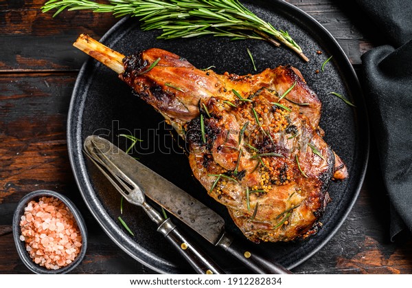 Baked lamb, sheep leg with rosemary. Dark wooden\
background. Top view