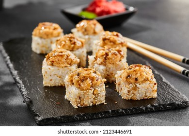 Baked Maki sushi on dark slate. Hot unagi maki with eel. Sushi roll with baked eel, cheese and unagi sauce topped. Style concept japanese menu with black background, leaves and hard shadow