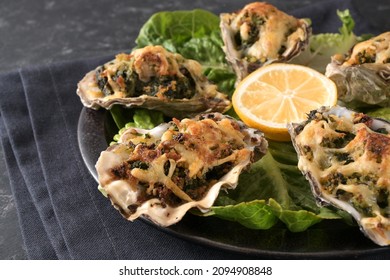 Baked oysters with spinach and cheese in Rockefeller style on a plate with lemon and lettuce, dark gray background, close up shot, selected focus, narrow depth of field