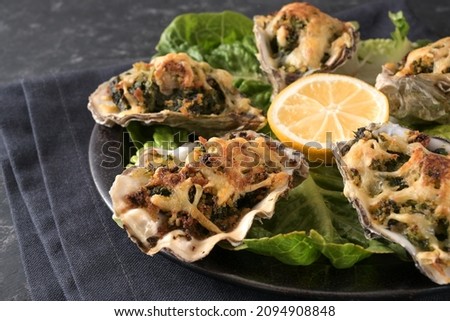 Baked oysters with spinach and cheese in Rockefeller style on a plate with lemon and lettuce, dark gray background, close up shot, selected focus, narrow depth of field