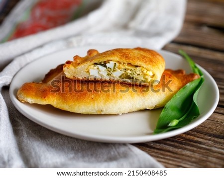 Baked patties or pies with ramson wild garlic, eggs and cheese. Homemade food. curd dough. Baking on a plate on wooden table with textile napkin, close-up. Local food