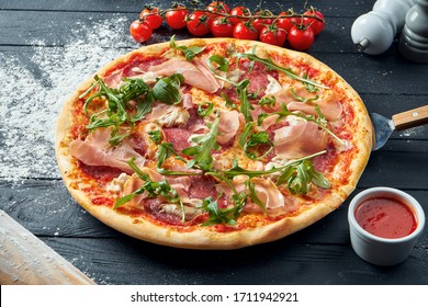 Baked Pizza With Salami, Prosciutto And Chicken With Red Sauce And Melted Cheese On A Black Wooden Background In A Composition With Ingredients. Top View