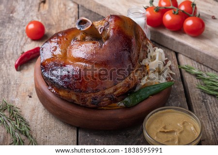 Baked pork knuckle on a wooden table with sauerkraut and fresh vegetables. A large portion of food. Close up