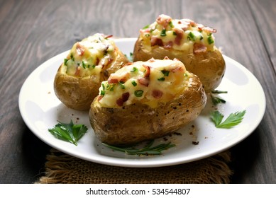 Baked potato with bacon, cheese and green onion on plate, close up view.