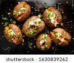 Baked potato, baked potatoes stuffed with butter, cream cheese and green onions, seasoned with freshly ground black pepper and sea salt flakes on a black background, top view