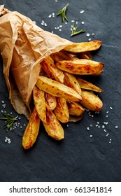 Baked potato wedges  with addition sea salt and rosemary on a black background, top view