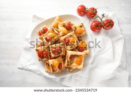 Baked puff pastry snacks with cream cheese, tomatoes and herb pesto, party finger food on a white plate, high angle view from above, copy space, selected focus