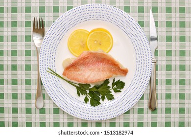 Baked RedFish Slices Of Lemon, Parsley, Plate, Knife & Fork On Green Plaid Table Cloth