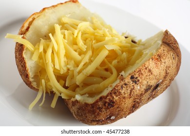 A Baked Russet Potato Stuffed With Grated Cheddar Cheese, On A White Plate