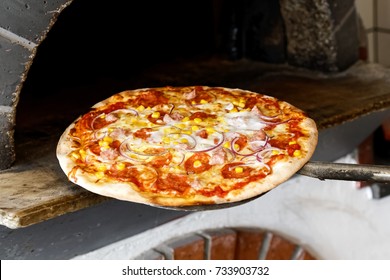 Baked Salami Pizza On Metal Paddle In Front Of Wood Oven.