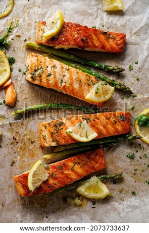Baked salmon and green asparagus with aromatic herbs and lemon slices on baking paper top view
